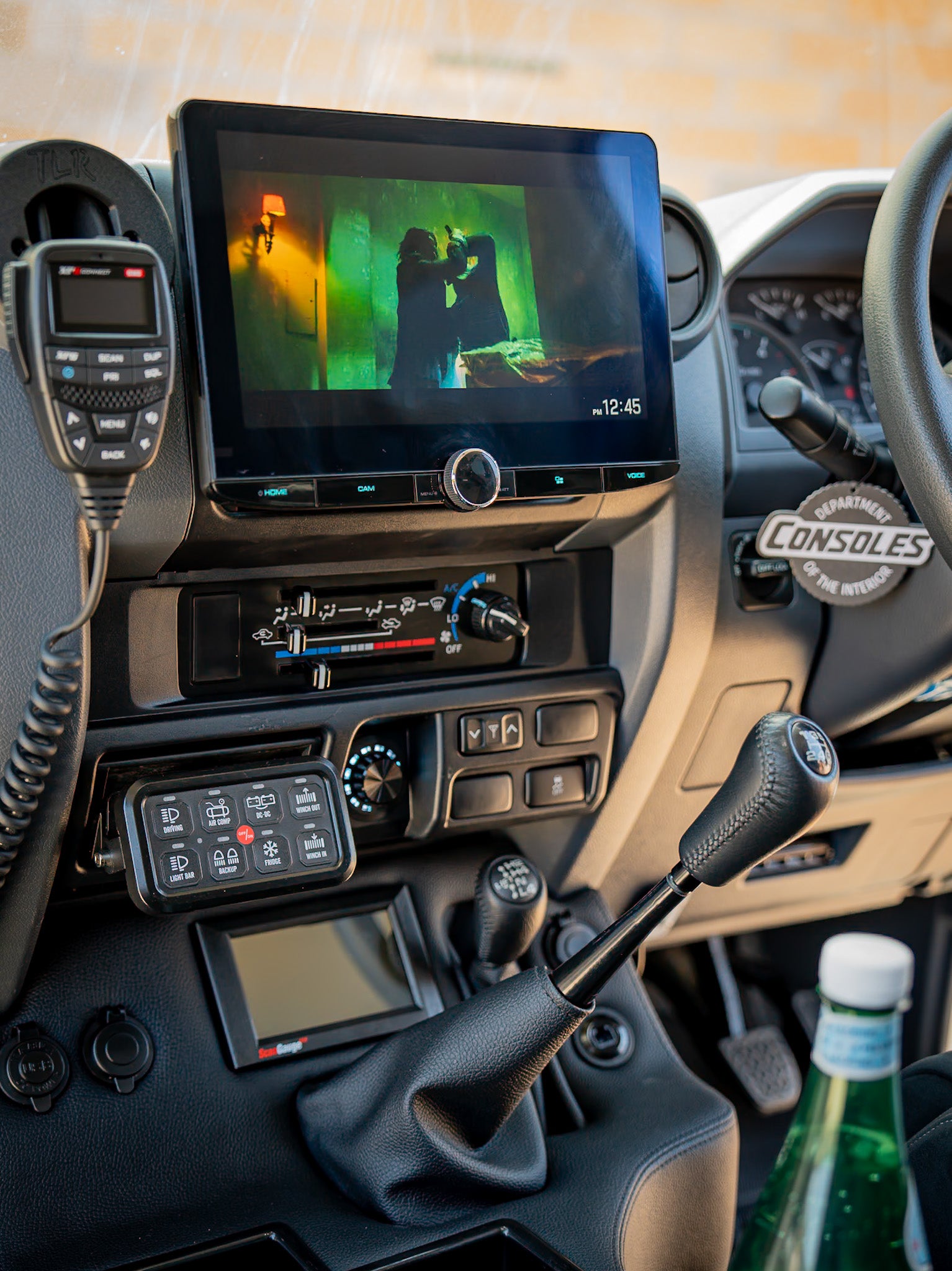 Car dashboard with a navigation screen displaying a movie, surrounded by various controls and a bottle.