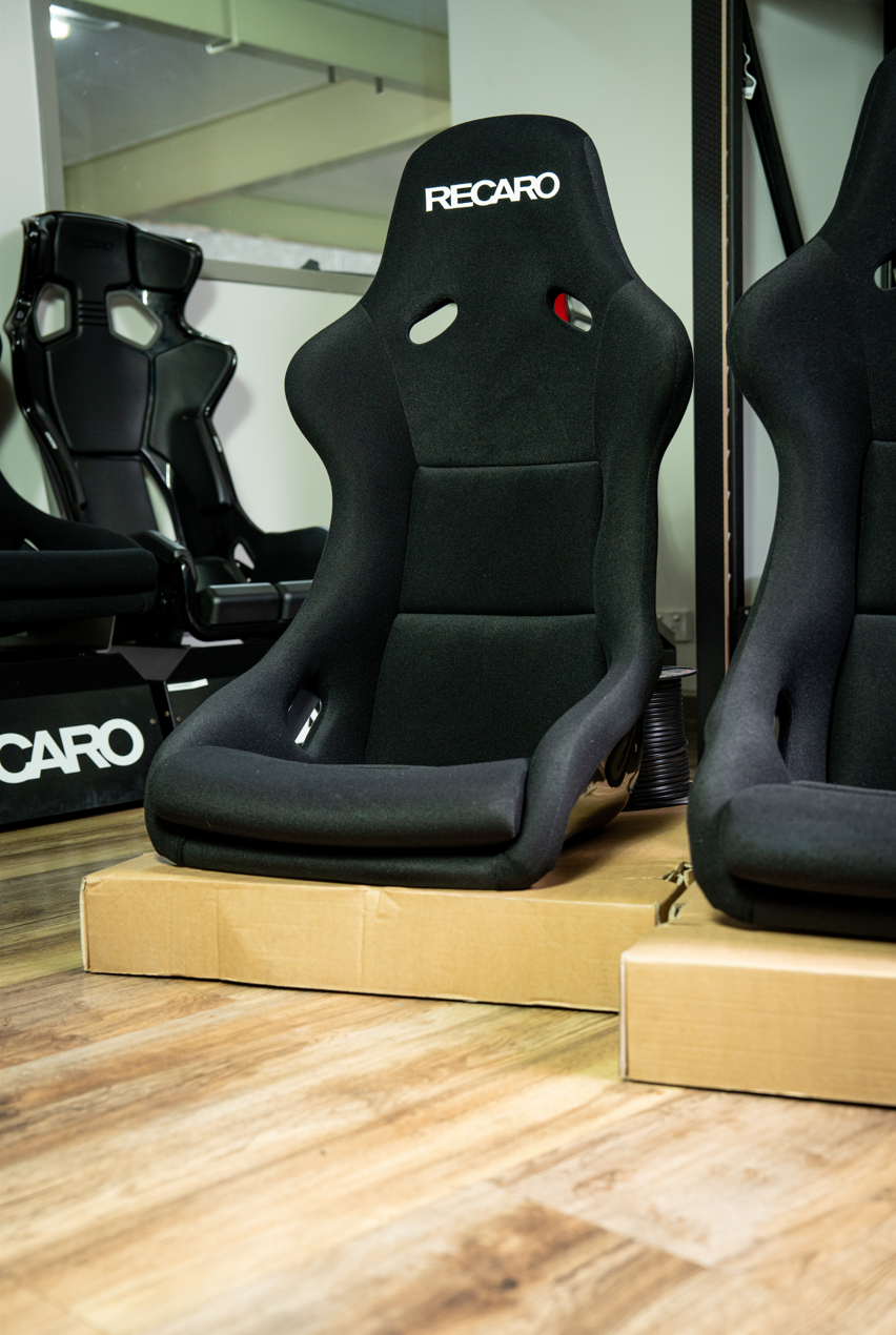 Black Recaro Pole Position racing seat on display with a reflective surface in the background